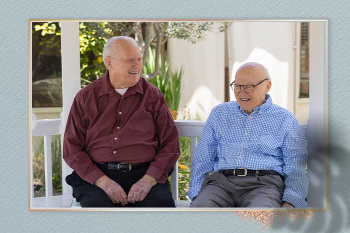 Two elderly gentlemen sitting on a bench in a gazebo chatting.